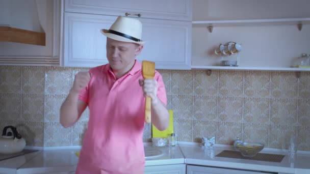 Hombre con camisa rosa y sombrero bailando y cantando en la cocina, emociones positivas — Vídeo de stock