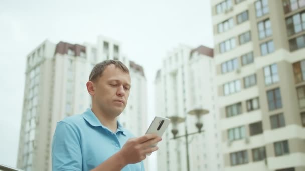Citizen naviga nel suo cellulare, scrive un messaggio di testo, fa da sfondo agli edifici della città — Video Stock