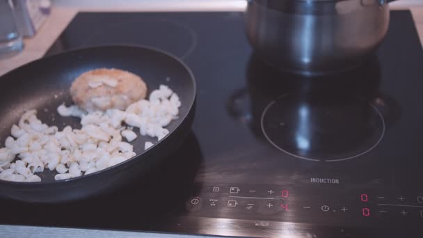 Жінка розігріває вечерю на сковороді на індукційній плиті — стокове відео