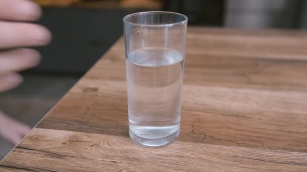 一只雄性手拿着一杯晶莹清澈的水，把它放回到一张木制桌子上，特写 — 图库视频影像