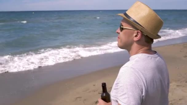 Turysta w kapeluszu stoi nad morzem i pije piwo, pomysł na wakacje — Wideo stockowe