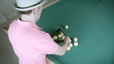 Bilardo oynayan, tişörtlü bir adam üçgen şeklinde top toplar.