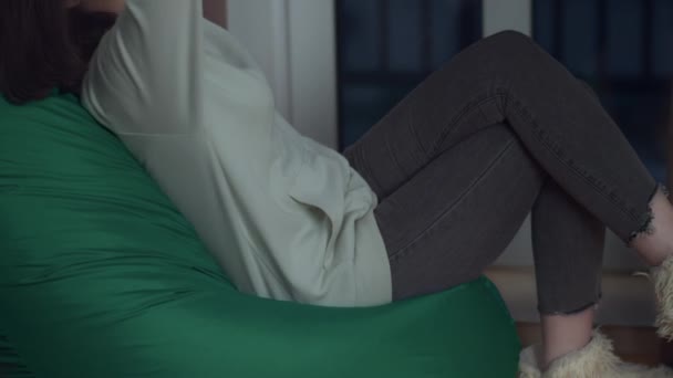 Chica en la noche en su habitación se sienta en una bolsa de frijoles lanzando las manos detrás de la cabeza, concepto de relajación — Vídeos de Stock