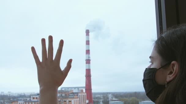 Μια κοπέλα με μαύρη μάσκα κοιτάει έξω από το παράθυρο και βάζει το χέρι της στο γυαλί. Ατμοσφαιρική ρύπανση — Αρχείο Βίντεο