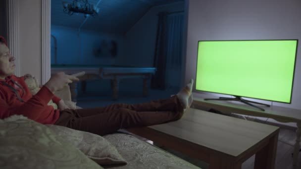 Lonely man at night sits at home on the couch with a remote control, switches channels, chroma key — Stock Video