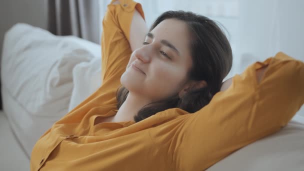 Portrait of a relaxed young girl sitting on the couch, raising her hands behind her head — Stock Video