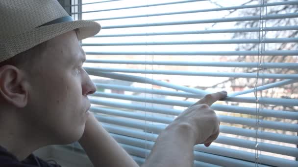 一个戴帽子的人，透过百叶窗看到街上发生的一切，他脸上的恐惧 — 图库视频影像