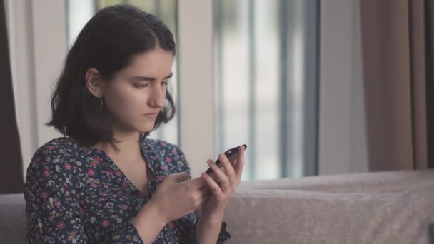Portrait d'une fille brune avec un téléphone portable dans ses mains, fond de fenêtre — Video