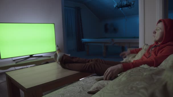 A man sits alone on the couch at night, watching TV — Stock Video