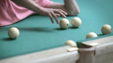 Bilardo masasında yatan bir adam bilardo toplarıyla oynar, onları cebine atar, yakın plan.