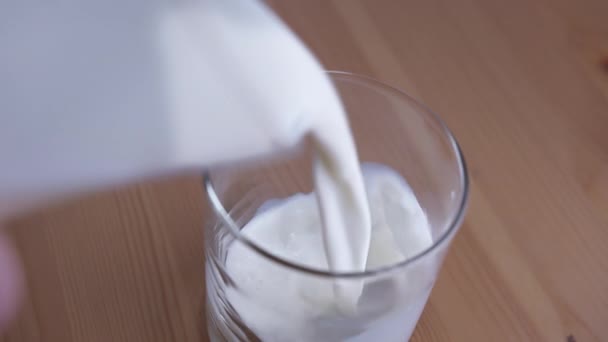 Tahta bir masanın üzerinde duran bardağa taze süt döküyorum. — Stok video