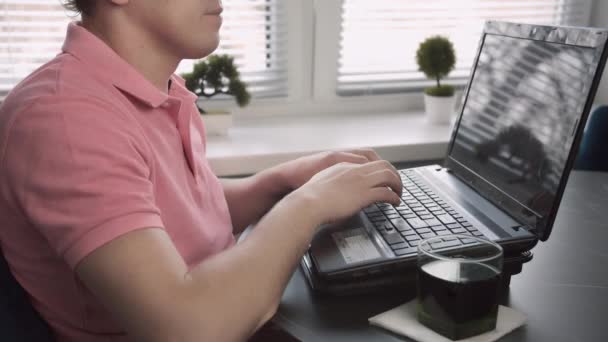 Freelancer sentado en la mesa y escribiendo texto en el portátil, fondo de ventana, oficina en casa, seguimiento de la cámara — Vídeos de Stock