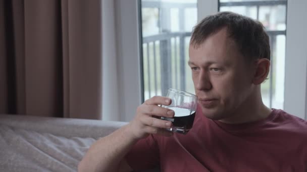 Uomo triste che beve alcol mentre è seduto sul divano, sfondo della finestra — Video Stock