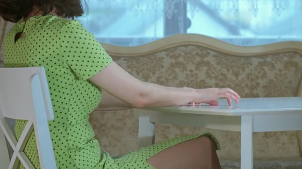 Mädchen sitzt am Tisch und tippt nervös auf ihre Finger, Fensterhintergrund — Stockvideo