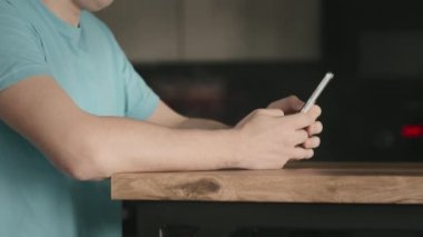 Elinde cep telefonu olan tişörtlü bir adam mobil uygulama kullanıyor.