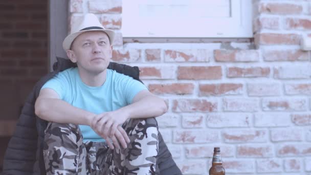 Man met hoed rust terwijl hij op de veranda van zijn huis zit, vakantie concept — Stockvideo
