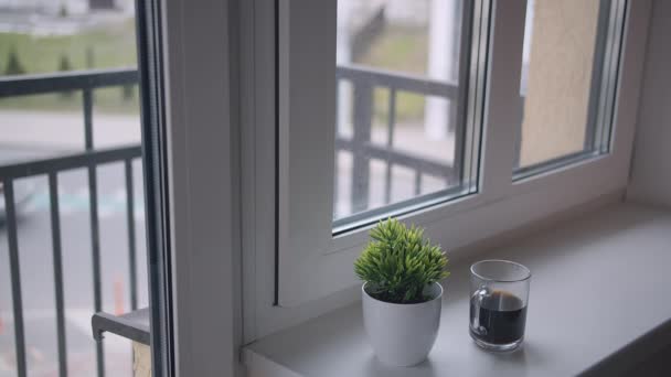 Una taza de café está en el alféizar de la ventana, fuera de la ventana hay tráfico — Vídeo de stock