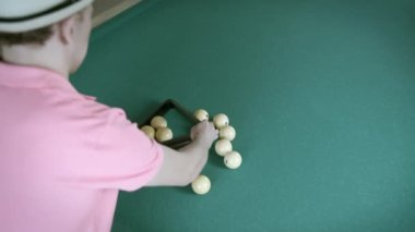Bilardo oynayan, pembe tişörtlü bir adam üçgen şeklinde top toplar.