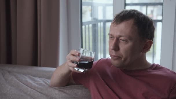 Ideges férfi iszik alkoholt, miközben ül a kanapén, ablak háttér — Stock videók