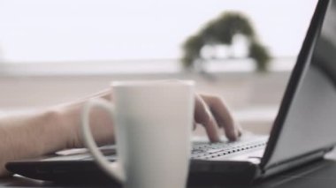 Erkeklerin elleri dizüstü bilgisayarda klavyeye yazı yazarken, kahve bardağının yanında, geçmişi bulanık.