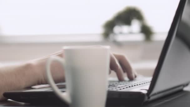 Hombres manos escribiendo en un teclado portátil, escribiendo texto, junto a una taza con café, fondo borroso — Vídeos de Stock