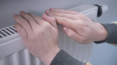 Isınma mevsimi olan bir aküye dokunarak ellerini ısıtır.
