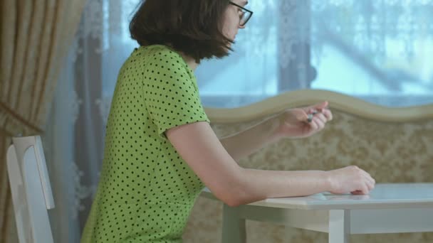 Brunetka dziewczyna w zielonej sukience je śniadanie siedząc przy stole w domu — Wideo stockowe