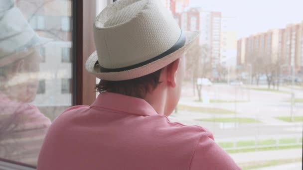 Vista desde atrás del hombre con sombrero con un vaso de bebida, mirando por la ventana abierta — Vídeos de Stock