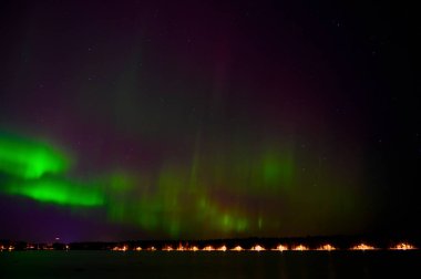 Aurora borealis yeşil ışık demeti. Mor kuyruklu. Yıldızlı gökyüzünün altında, İskandinav ülkesinde yansıyan bir göl.