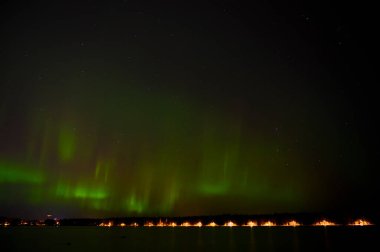 Yıldızlı gökyüzünün altında mor kuyruklu yeşil Aurora Borealis ışıkları, İskandinav ülkesini yansıtıyor.