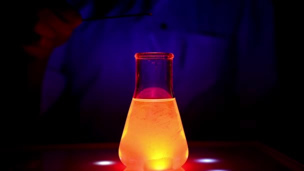 科学者は青い光の下で磁気攪拌機に赤い色の溶液を混合している薬化学のための化学研究所で混合の圧延運動と — ストック動画