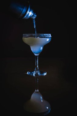 Buzlu Margarita kokteyli, tekila ve limon şurubuyla karıştırılmış kokteyl bardağından buz küpleriyle doldurulmuş, limon ve samanla süslenmiş ve Noel gecesi tuzlu jantla süslenmiş.