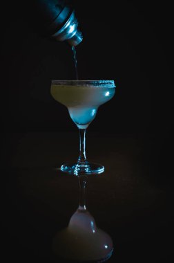 Buzlu Margarita kokteyli, tekila ve limon şurubuyla karıştırılmış kokteyl bardağından buz küpleriyle doldurulmuş, limon ve samanla süslenmiş ve Noel gecesi tuzlu jantla süslenmiş.