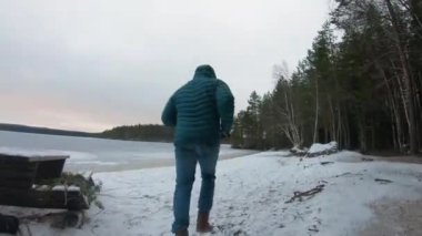 Kışın donmuş gölün kenarında koşan kışlık ceket giyen bir adam.