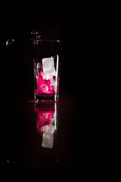 完全な暗い背景に対してガラスに氷の上に赤の非アルコール溶液の流れを注ぐ コピースペース アルコール ワイナリーのコンセプトを注ぐ — ストック写真