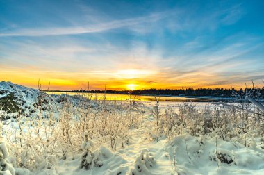 Gün batımının panoramik görüntüsü. Kış boyunca bir deniz sahilinde parlayan karlar arasında.