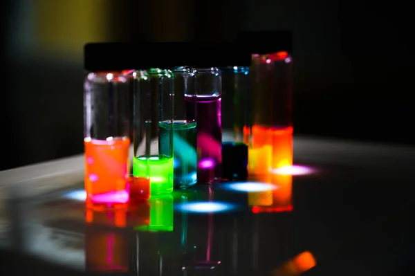 Various colourful analytical sample in glass vial in an inorganic chemistry laboratory experiment on the UV light by a woman scientist