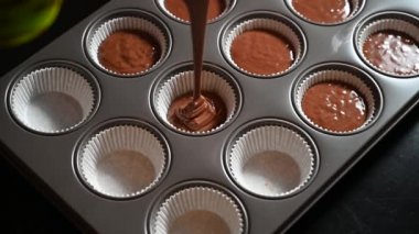 Human hand Pouring chocolate cake batter into a multiple metal cupcake pan. Chocolate cupcakes or muffins dough Pouring into Cup Molds 4K video