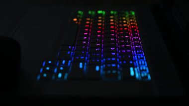 RGB ışıklandırmalı klavye sanal video oyunları için renk değiştiriyor ve karanlık ofis odasındaki güçlü bilgisayarda düzenleme yapıyor. Modern teknolojide gökkuşağı tayfı.