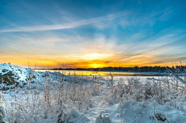 Gün batımının görkemli manzarası. Kış boyunca bir deniz sahilinde parlayan karlar arasında.