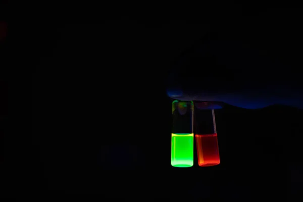 A woman researcher holding chemistry photochemical reaction glowing glass vials in a organic laboratory - radioactive - fluorescence. A copy space black background. Medicinal chemistry laboratory.