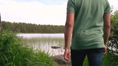 Coronavirus Covid-19 salgınından sonra temiz hava almak için maskesini çıkarıp gölün kenarında oturan adamın 4K videosu.
