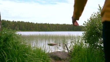 Coronavirus Covid-19 salgınından sonra temiz hava almak için maskesini çıkarıp gölün kenarında oturan adamın 4K videosu.