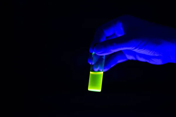 A scientist holding chemistry photochemical reaction green glass vials in a organic laboratory. A copy space black background. Medicinal chemistry laboratory.