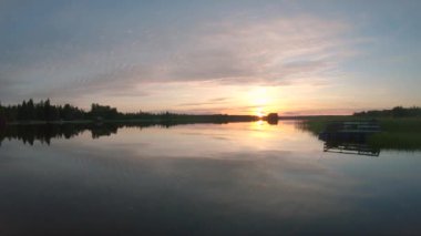 Gün batımı ve hareket eden bulutların altındaki turuncu gökyüzü ile birlikte büyüleyici panoramik göl manzarası. 2K yavaş çekim Kuzey Gölü manzarası. Güneş ufukta sakin bir manzarada batar.
