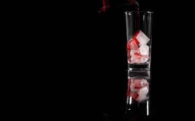 Alkolsüz kırmızı solüsyon akışını buzun üstüne koyu arkaplana karşı bardağa döküyor. kopyalama alanı. İçki, şarap konsepti.