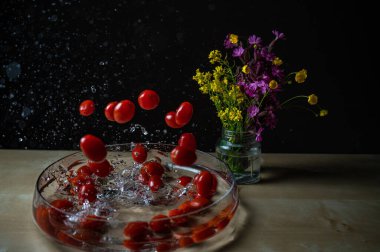 Taze organik kırmızı erik domatesleri (bebek domates, kiraz domatesleri) su kabına su sıçratan bir grup.