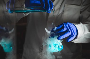 Mavi renk çözeltisiyle dumanlı deneyler. Kimyasal reaksiyon üzerinde çalışan bilim adamı cam şişeden yoğun duman çıkarıyor. Kopyalama alanı