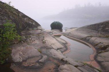 Adanın taş kıyısındaki sisin içinde bir tekne.