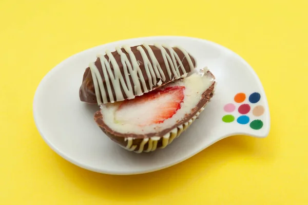 Chocolate egg (Easter egg) coconut stuffed with strawberry sliced in half on a plate. Isolated on yellow background. Close-up.